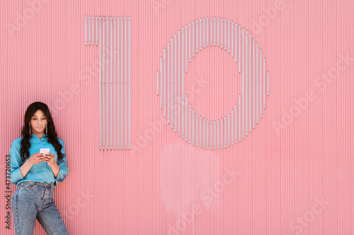 Female transgender using mobile phone by number 10 on pink corrugated wall photo