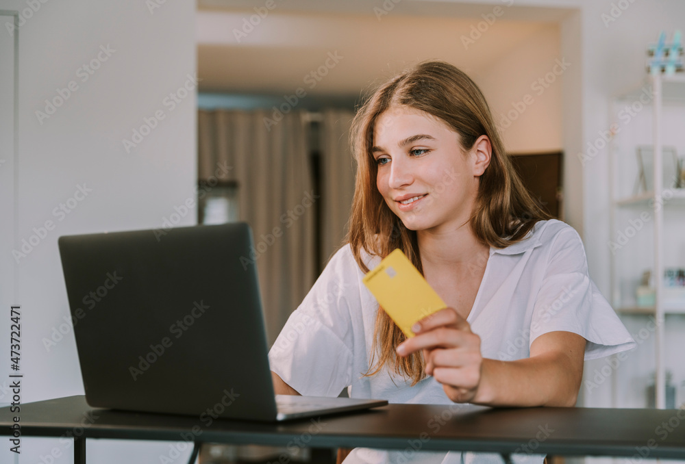 Female student holding credit card while using laptop at home Female student holding credit card while using laptop at home