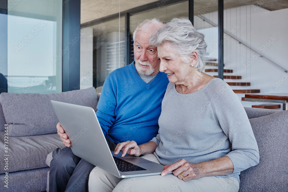 Surprised man looking at laptop used by woman while sitting in living room Surprised man looking at laptop used by woman while sitting in living room