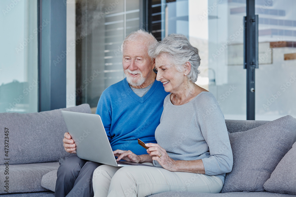 Smiling senior couple doing online shopping while sitting in living room at home Smiling senior couple doing online shopping while sitting in living room at home