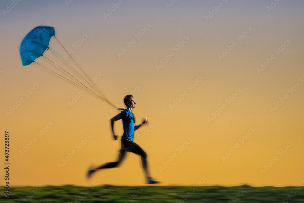 Male sportsperson jogging with parachute during sunset Male sportsperson jogging with parachute during sunset