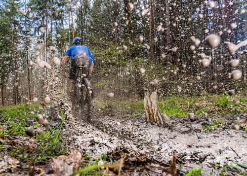 Young man riding mountain bike through mud in forest