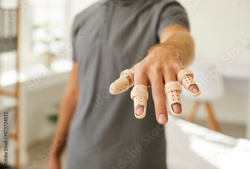 Man who has hurt his fingers is wearing adjustable finger splint braces. Close up shot of a guy showing his hand with beige support braces on his injured fingers and thumb. Injury treatment concept