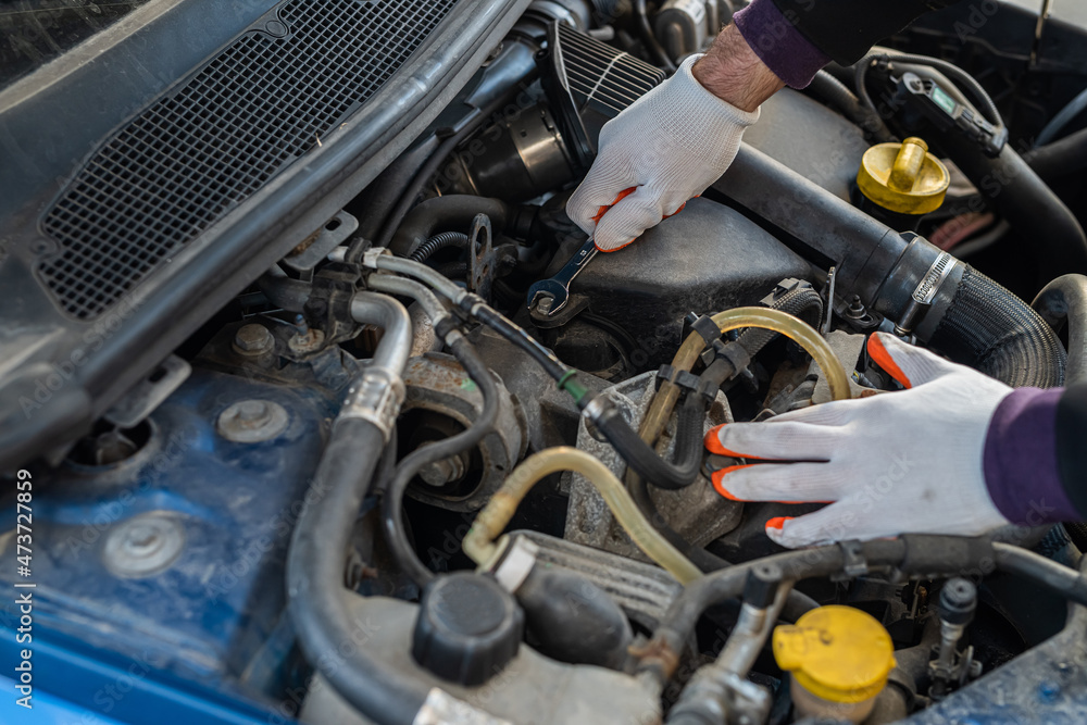 hands of a strong man mechanic in gloves repairs the car under the hood. hands of a strong man mechanic in gloves repairs the car under the hood.
