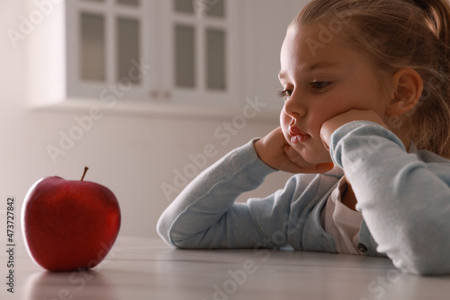Cute little girl refusing to eat apple in kitchen photo