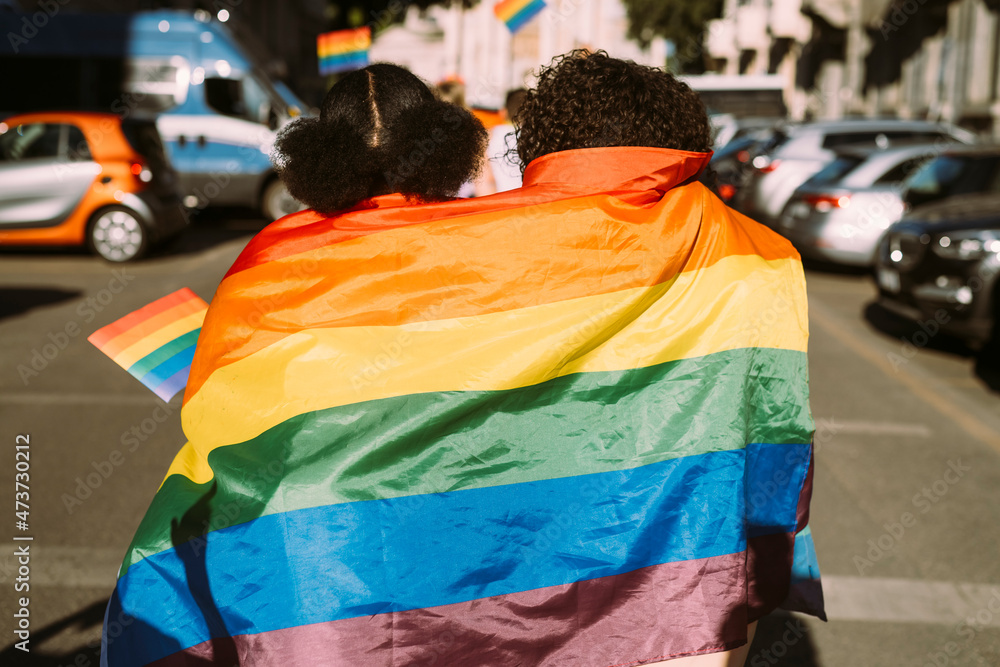 Female friends wrapped in rainbow flag on sunny day Female friends wrapped in rainbow flag on sunny day