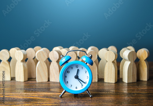 Alarm clock and a crowd of people. Time management. Hourly wages, strict work limits and break time. Planning and forecasting. Employee performance monitoring system, Organization of business photo