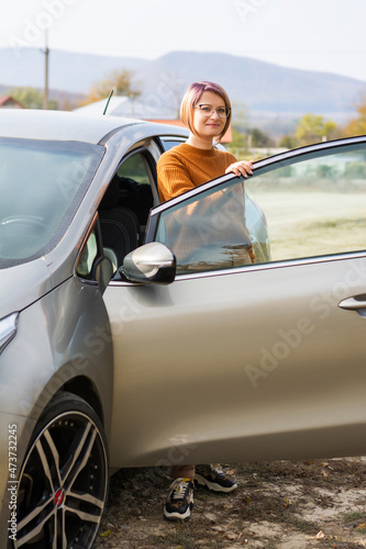 Confident business woman in brown sweater and glasses staying next to the car in the forest