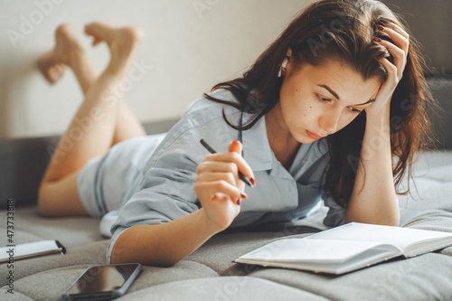 Image of a woman lying on a bed at home in a bedroom in casual clothes, with a diary book, a planner and a pen.