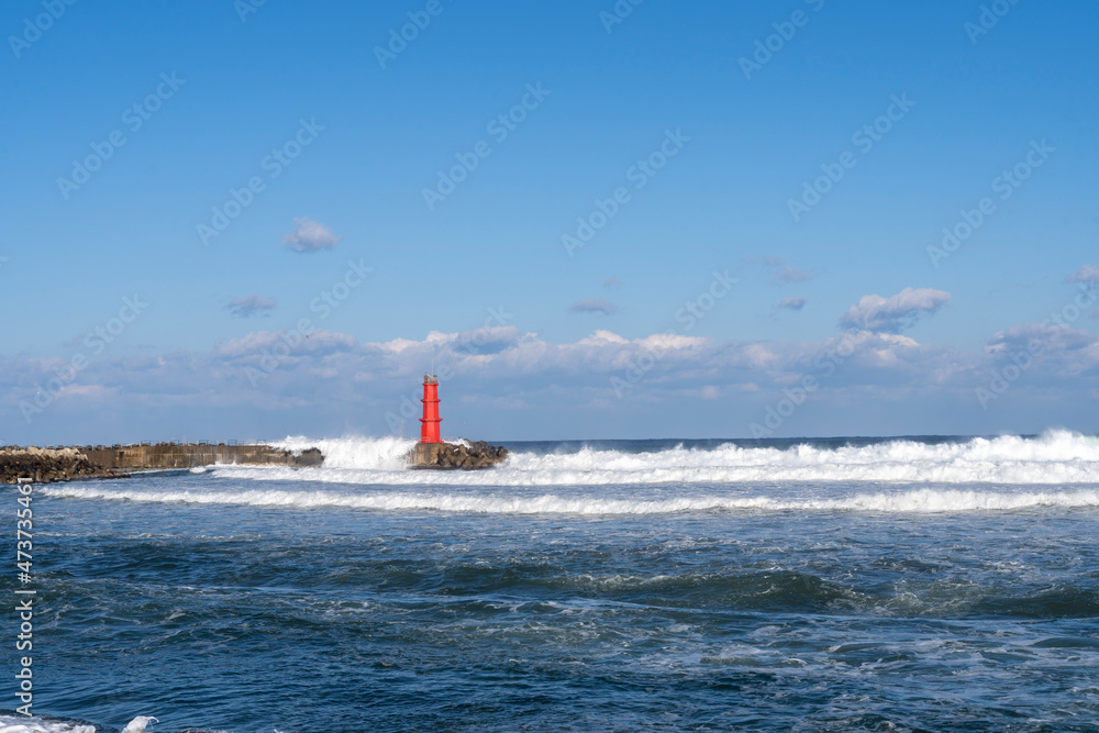 Red lighthouse and waves in the winter sea