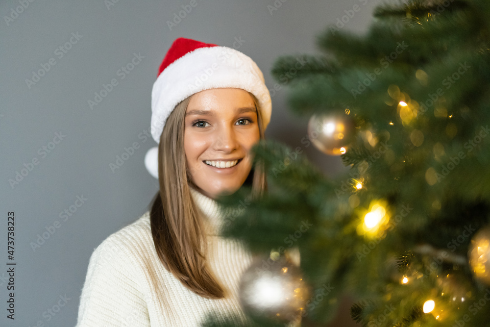 Young woman in santa claus hat posing near Christmas tree. Winter holiday, vacation, relax and lifestyle concept. Young woman in santa claus hat posing near Christmas tree. Winter holiday, vacation, relax and lifestyle concept.