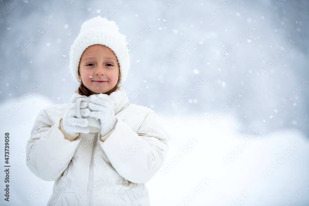 a little girl in a white jacket and a white hat is holding a cup of tea in her hands during a snowfall against the backdrop of beautiful snowdrifts and forests a little girl in a white jacket and a white hat is holding a cup of tea in her hands during a snowfall against the backdrop of beautiful snowdrifts and forests