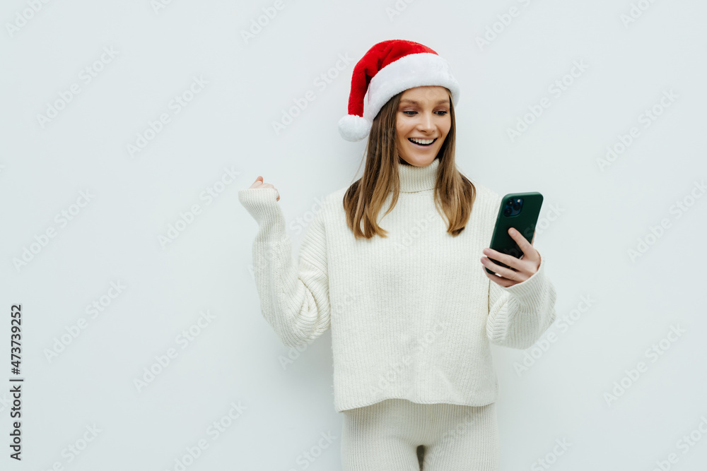 Beautiful young woman with christmas hat hoding phone with win gesture on white background. Beautiful young woman with christmas hat hoding phone with win gesture on white background.