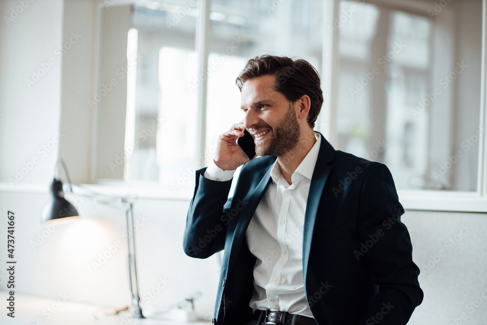 Smiling businessman talking on smart phone at office Smiling businessman talking on smart phone at office