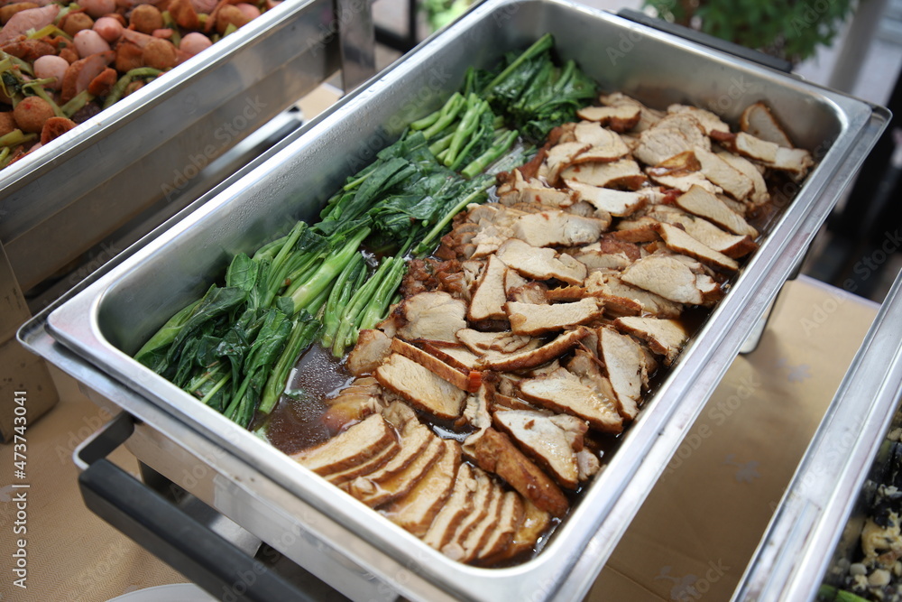 Roast Pork with Vegetables, food in buffet line. The container is a rectangular stainless steel tray. Selective focus.