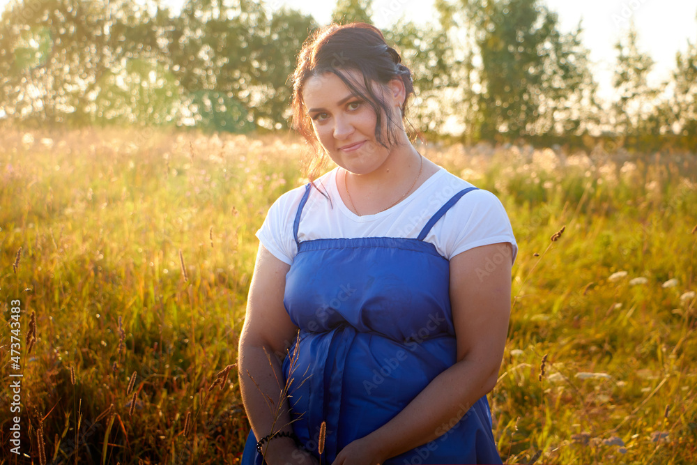 Peasant plump chubby pleasant woman in green grass field. Girl in blue old russian dress posing outdoors in nature in a day or a evening Peasant plump chubby pleasant woman in green grass field. Girl in blue old russian dress posing outdoors in nature in a day or a evening