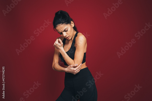 Mid adult sportswoman with pain in elbow against maroon background photo