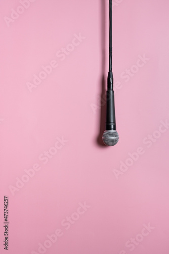 Modern black wired mic hanging on pink background and casting shadow in studio. Concept of voice of women