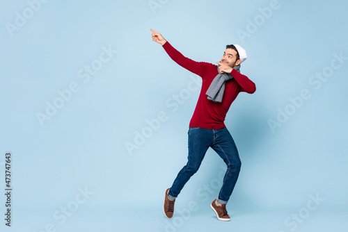 Young happy handsome Caucasian man wearing Christmas attire dancing and pointing hands up in isolated light blue background