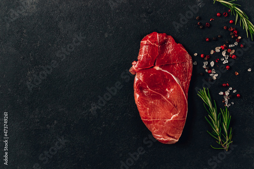 raw beef steak with rosemary and peppers on dark stone