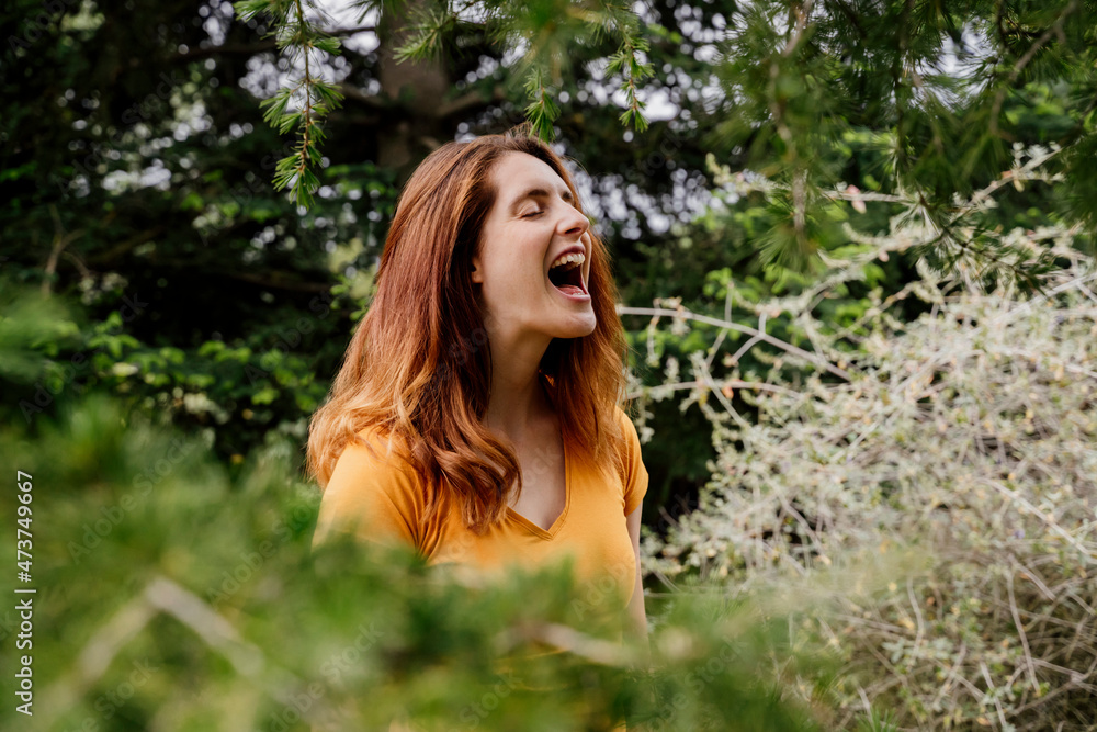 Redheaded woman screaming in garden with mouth open Redheaded woman screaming in garden with mouth open