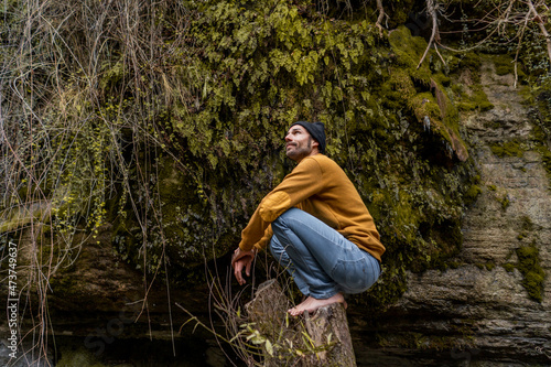 Thoughtful male hiker crouching on tree stump in forest photo
