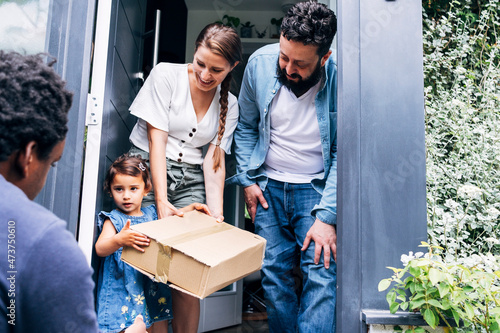 Smiling parents looking at daughter receiving package from delivery person photo