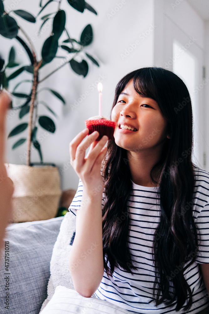 Smiling young woman holding cupcake with candle at home Smiling young woman holding cupcake with candle at home