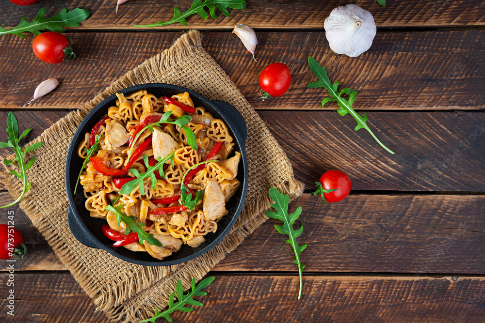 Tasty pasta in tomato sauce with chicken, pepper and herbs on wooden background. Top view