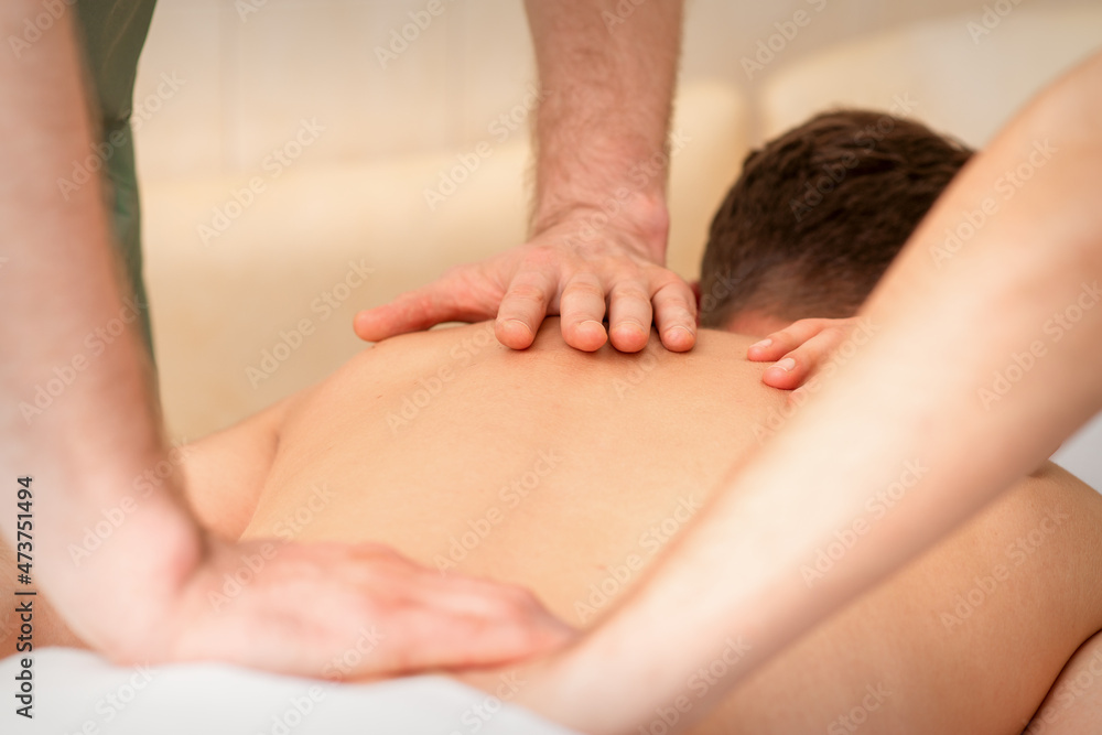 Young man receiving back massage in four hands in spa beauty salon Young man receiving back massage in four hands in spa beauty salon