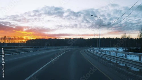 View through the windshield of a moving car on the road with a fence and a beautiful sunrise in the winter sky.