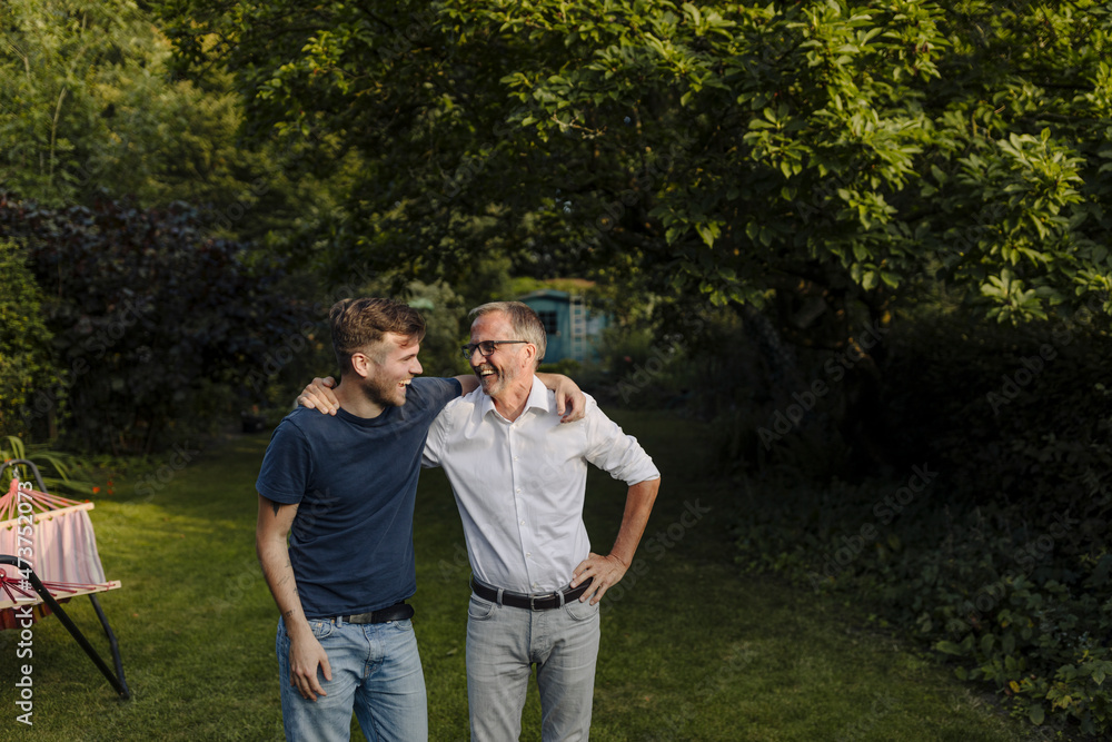 Laughing son and father with arm around standing in back yard Laughing son and father with arm around standing in back yard