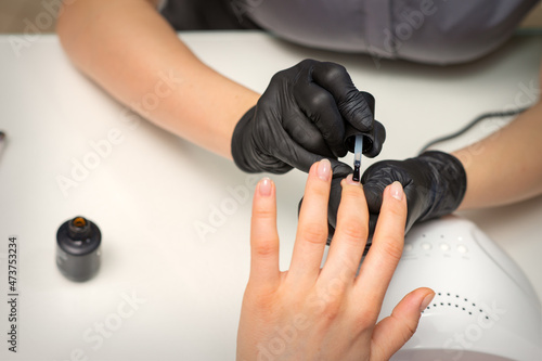 Painting nails of a woman. Hands of Manicurist in black gloves applying transparent nail polish on female Nails in a beauty salon
