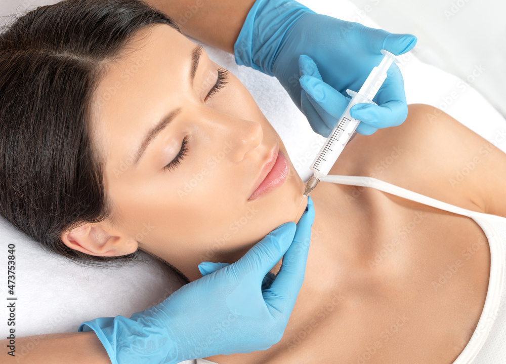 Cosmetologist makes lipolytic injections to burn fat on the chin, cheeks and neck of a woman against double chin. Female aesthetic cosmetology in a beauty salon.Cosmetology concept. Cosmetologist makes lipolytic injections to burn fat on the chin, cheeks and neck of a woman against double chin. Female aesthetic cosmetology in a beauty salon.Cosmetology concept.