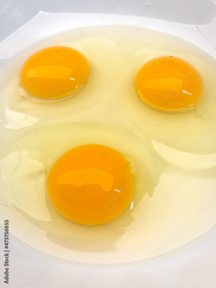 Three bright yellow raw chicken eggs in a white bowl. Three bright yellow raw chicken eggs in a white bowl.