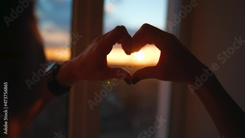 hands forming a heart shape with sunset silhouette