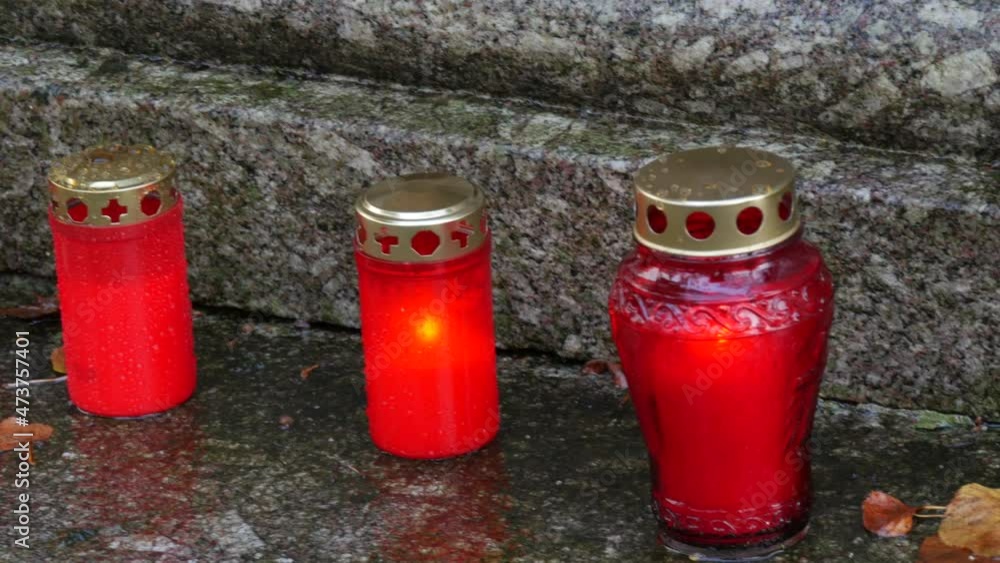Row red memorial candle burning with fire on rainy day on tombstone in cemetery autumn, rainy day. Grave with tombstone on which raindrops falling. Day of all dead Row red memorial candle burning with fire on rainy day on tombstone in cemetery autumn, rainy day. Grave with tombstone on which raindrops falling. Day of all dead