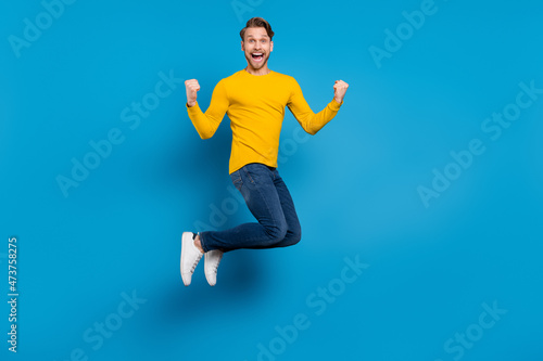 Full length body size of young guy smiling jumping up gesturing like winner isolated bright blue color background
