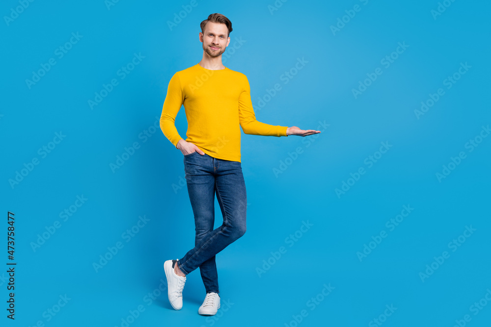 Fototapeta premium Full length body size of young guy smiling keeping blank space on hand isolated vibrant blue color background