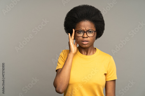 Shocked black female look surprised and astonished touching glasses with open mouth. Frustrated african woman hear unexpected bad news  horrified isolated over gray studio wall. Astonishment and shock