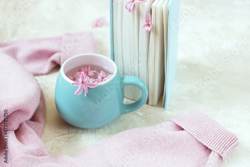 Fototapeta Naklejka Na Ścianę i Meble -  Cup with a drink, fresh flowers bookmarks in an open book, woolen pink sweater on a light background, top view, romantic congratulation, love emotion