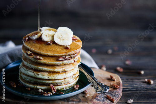 Maple syrup pouring onto pancakes served with fresh banana fruit and nuts. Selective focus with blurred background and foreground. photo