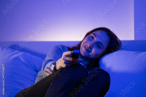 beautiful woman changing channels with remote, redhead young woman eating fruit while watching tv in her home