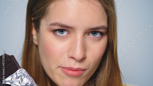 Closeup sensual woman enjoying chocolate at camera on grey background.