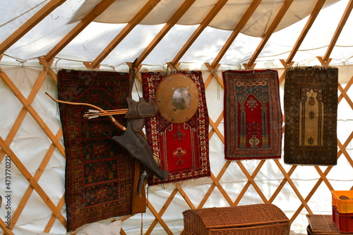 A close up on various decorative medieval rugs, shields, quivers, and arrows hanging from the beams of a rural tent or camp made out of cloth and wooden sticks seen on a Polish countryside in summer