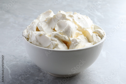 Bowl of tasty cream cheese on light grey marble table, closeup