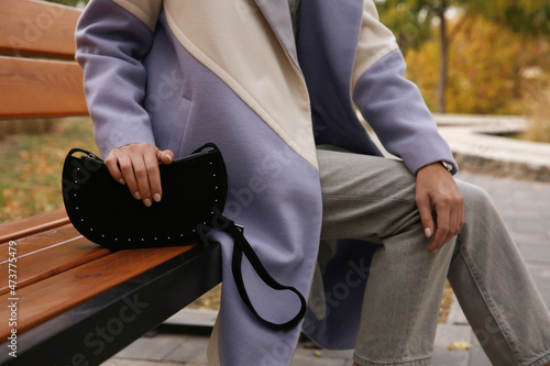 Stylish woman with trendy black baguette bag on bench in park, closeup