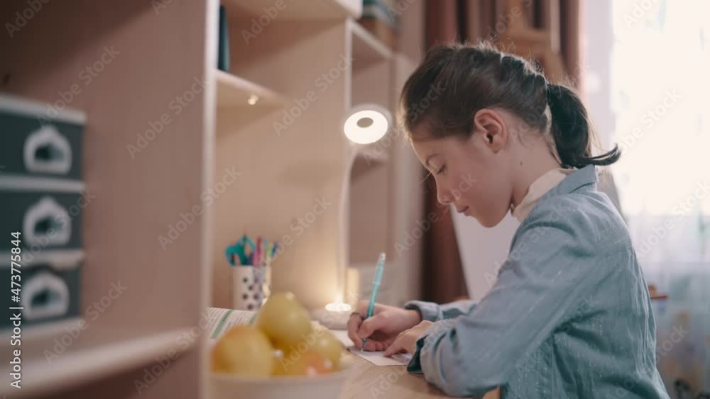 Girl doing homework. Girl writes in notebook at table in her room. Girl doing homework. Girl writes in notebook at table in her room.