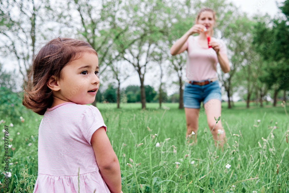 Daughter looking away while mother standing on grass at park Daughter looking away while mother standing on grass at park