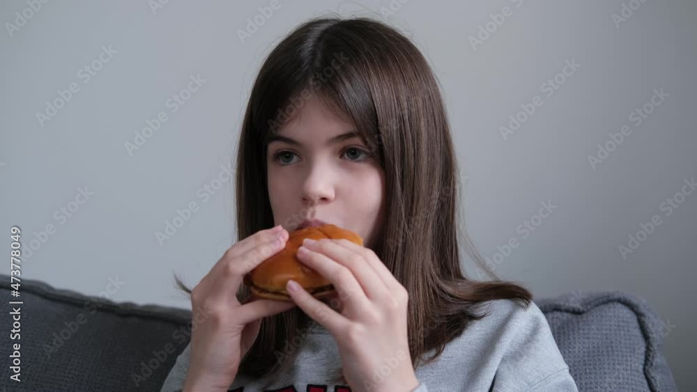 little girl, teenager eating burger at home on the couch. not healthy food, fast food concept little girl, teenager eating burger at home on the couch. not healthy food, fast food concept